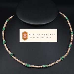 May include: A necklace featuring a strand of small, light-colored shell beads interspersed with vibrant green turquoise stones. The necklace is displayed on a black stand, with a label that reads "ROSLYN SANCHEZ JEWELRY DESIGNER".