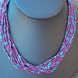May include: A multi-strand necklace made of small purple and blue beads. The necklace is displayed on a black mannequin bust.