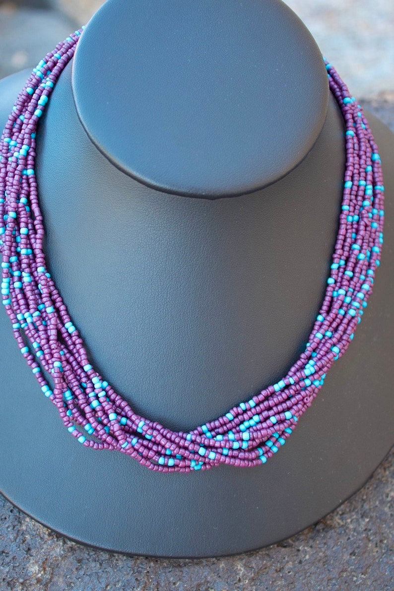 May include: A multi-strand necklace made of small purple and blue beads. The necklace is displayed on a black mannequin bust.