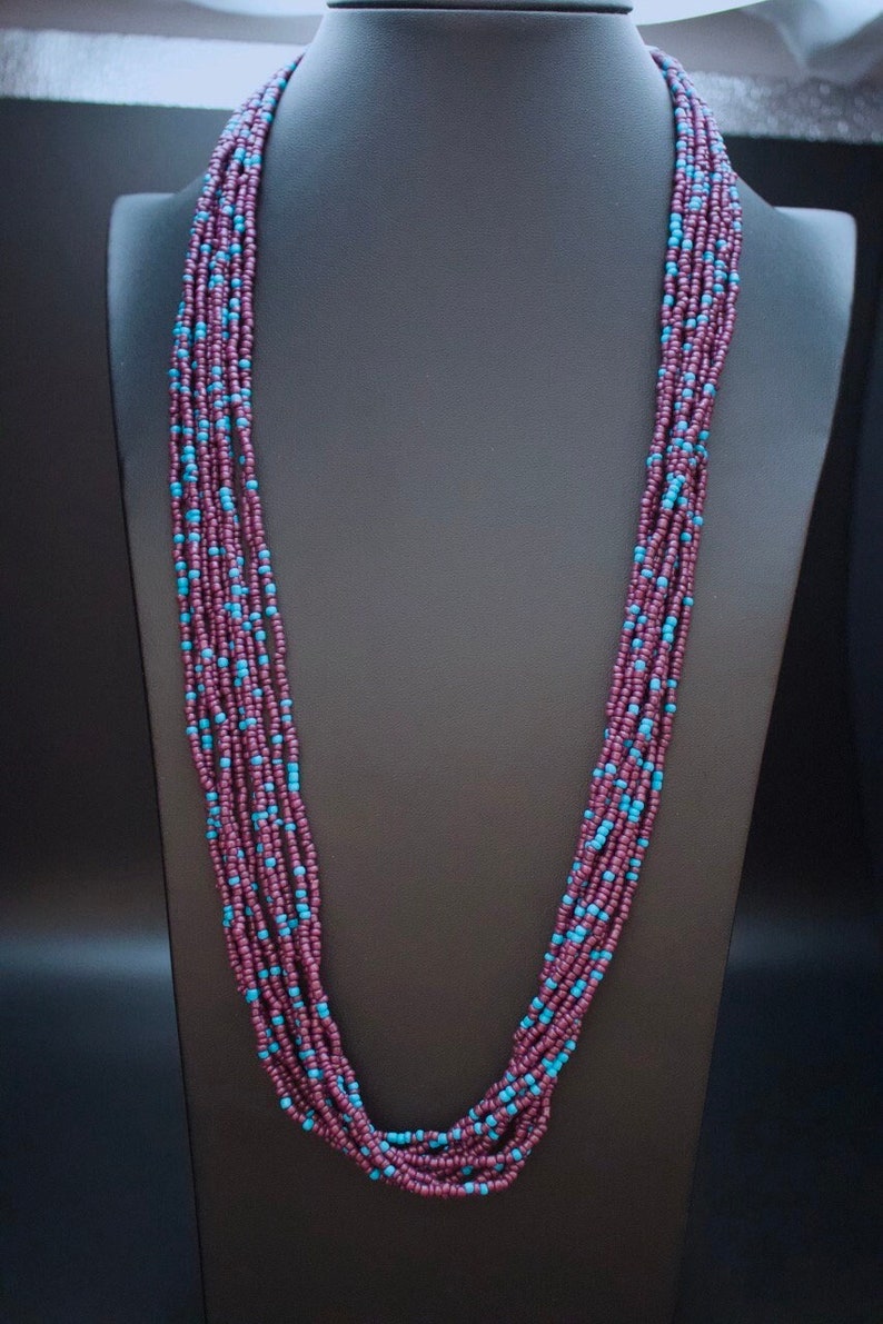 May include: A long multi-strand necklace made of small purple and turquoise beads. The necklace is displayed on a black mannequin.