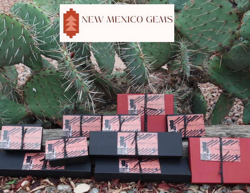 May include: A collection of small, black and red boxes with the text "New Mexico Gems" on them. The boxes are stacked on top of each other and are sitting on a wooden surface.