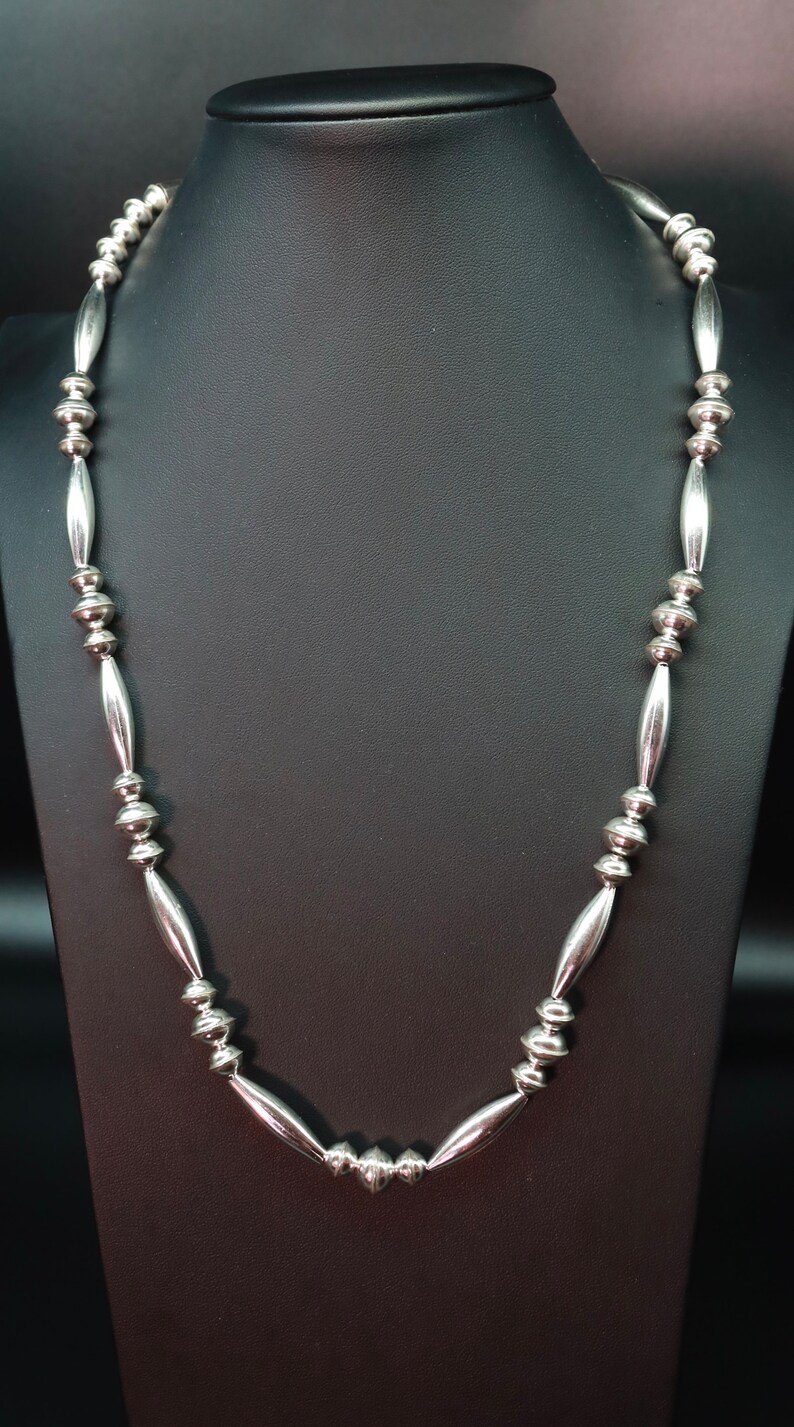 May include: A silver necklace with a repeating pattern of round and oval beads.