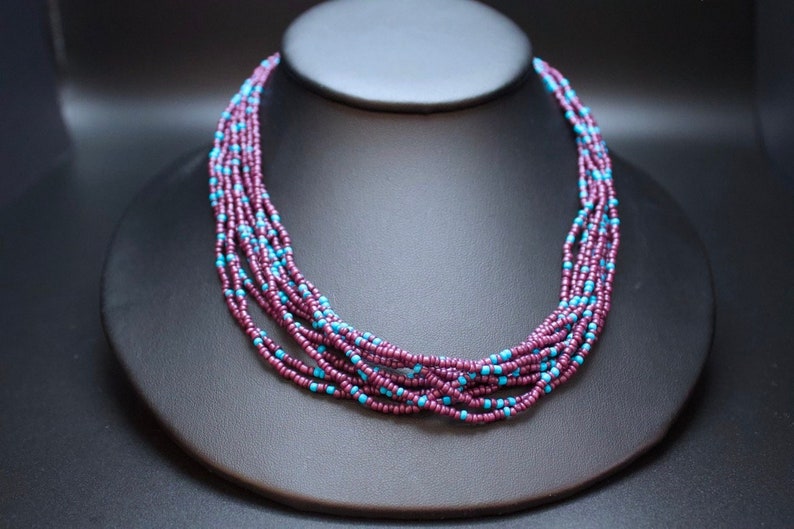 May include: A multi-strand necklace made of small, dark purple and turquoise beads. The necklace is layered and has a simple, elegant design.