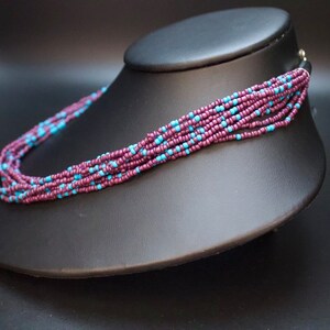 May include: A multi-strand necklace made of small, dark purple and light blue beads. The necklace is displayed on a black mannequin bust.