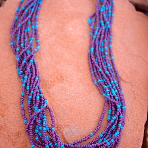 May include: A multi-strand necklace made of purple and turquoise beads. The necklace is made of small, round beads and has a silver clasp.