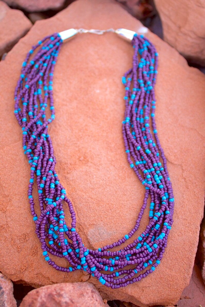 May include: A multi-strand necklace made of purple and turquoise beads. The necklace is made of small, round beads and has a silver clasp.