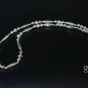 May include: A silver necklace with alternating round and elongated beads. The necklace is made of sterling silver and has a simple clasp.