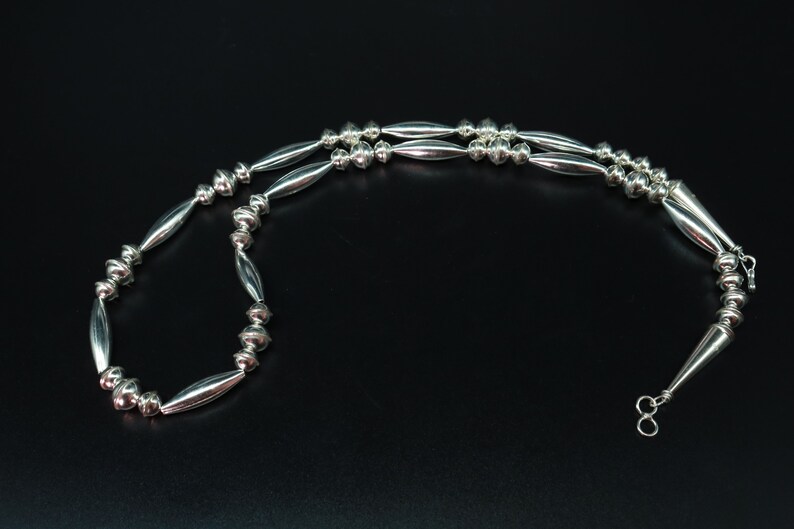 May include: A silver necklace with alternating round and elongated beads. The necklace is made of sterling silver and has a simple clasp.