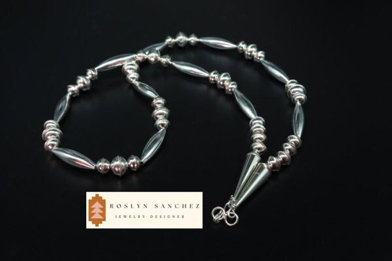 May include: A silver necklace and bracelet set with alternating round and oval beads. The necklace has a pointed pendant.