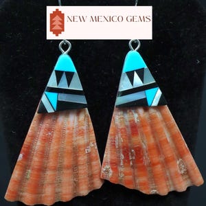 May include: A pair of handcrafted earrings featuring a triangular turquoise, black, and white inlaid design atop a fan-shaped, orange-hued shell. The earrings are suspended from silver-colored hooks. The text "NEW MEXICO GEMS" is displayed above the earrings.