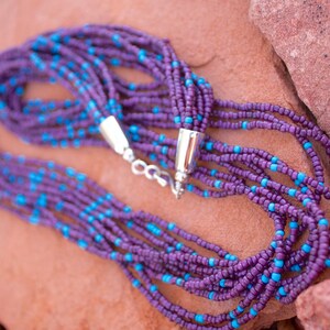 May include: A multi-strand necklace made of purple and turquoise beads. The necklace is made of small, round beads and has a silver clasp.