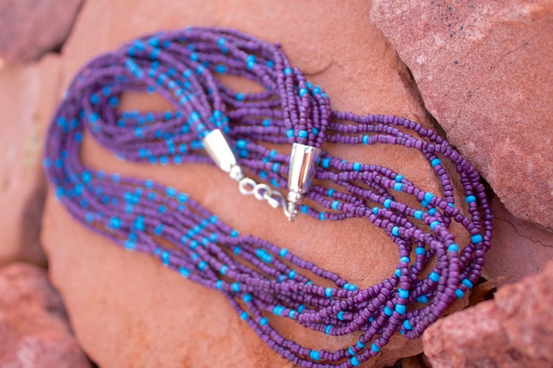 May include: A multi-strand necklace made of purple and turquoise beads. The necklace is made of small, round beads and has a silver clasp.