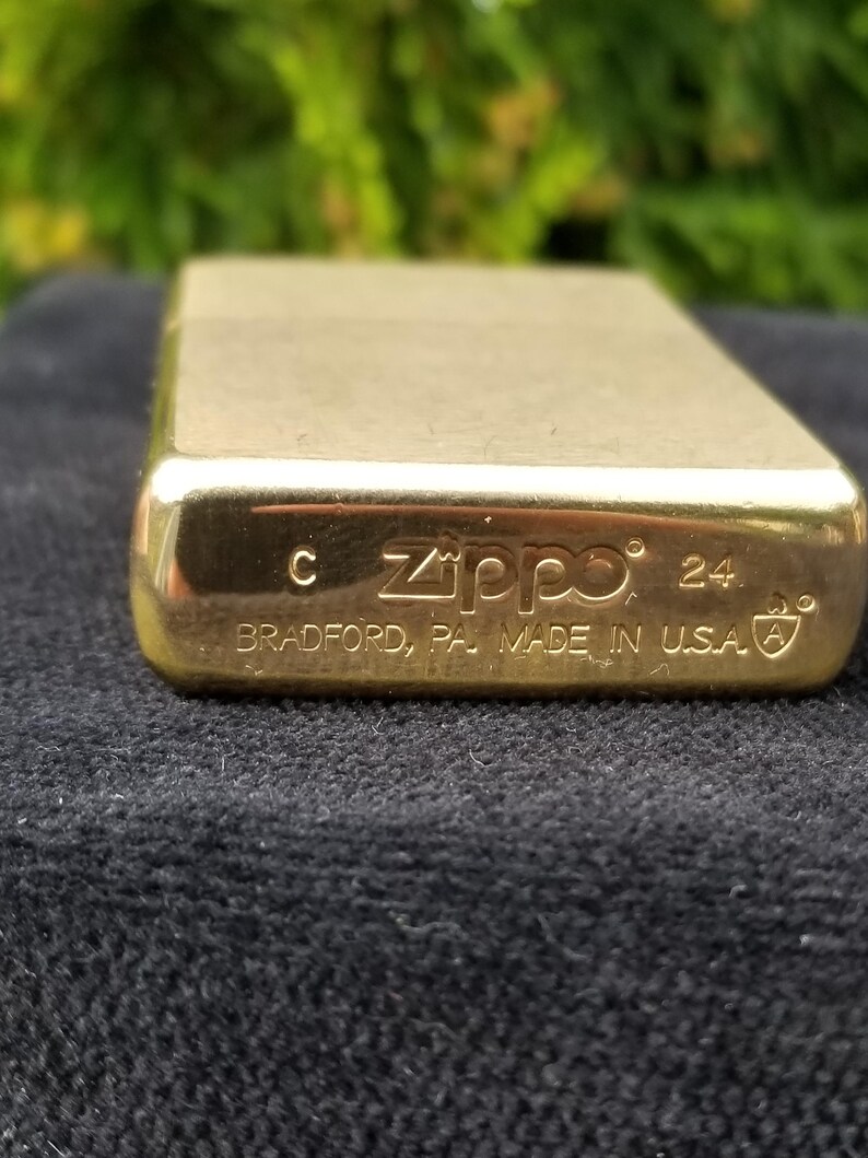 以下が含まれることがあります： 底面に「Zippo」と「Bradford, PA Made in USA」が刻印された金色のジッポーライター。ライターには「24」という数字と「C」という文字が刻印されています。