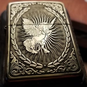 以下が含まれることがあります： 月桂樹の輪で囲まれた太陽の光の中に、羽根の生えた馬が刻まれた銀色のライター