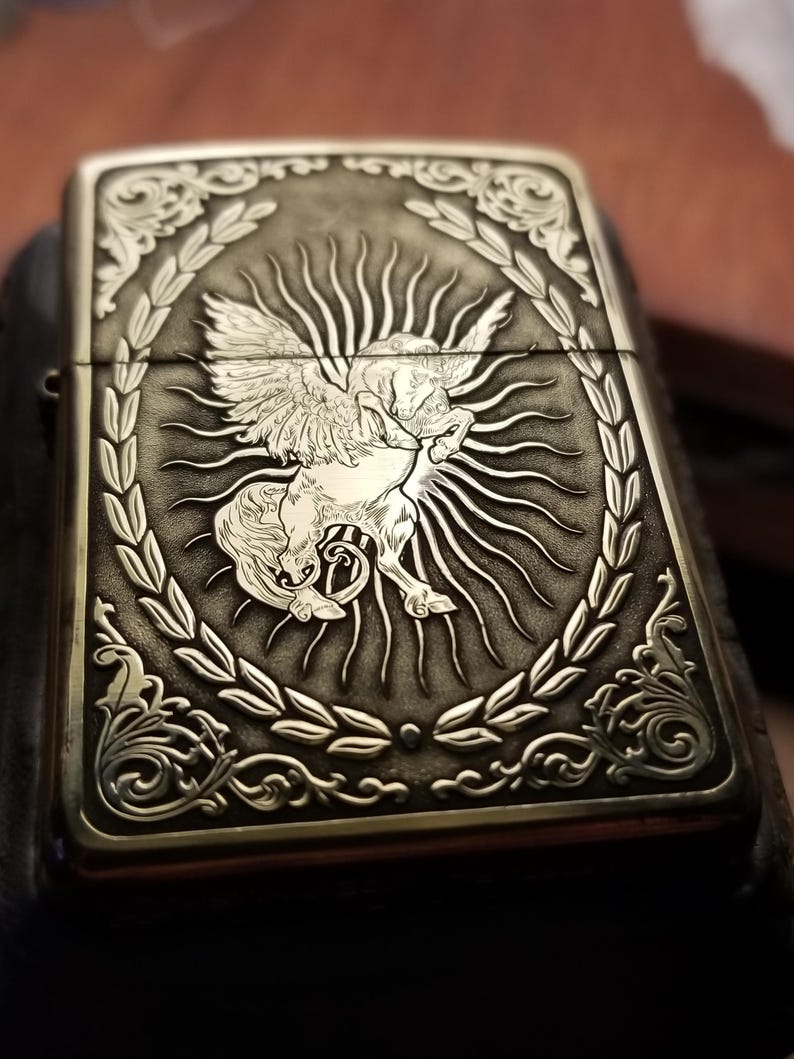 以下が含まれることがあります： 月桂樹の輪で囲まれた太陽の光の中に、羽根の生えた馬が刻まれた銀色のライター