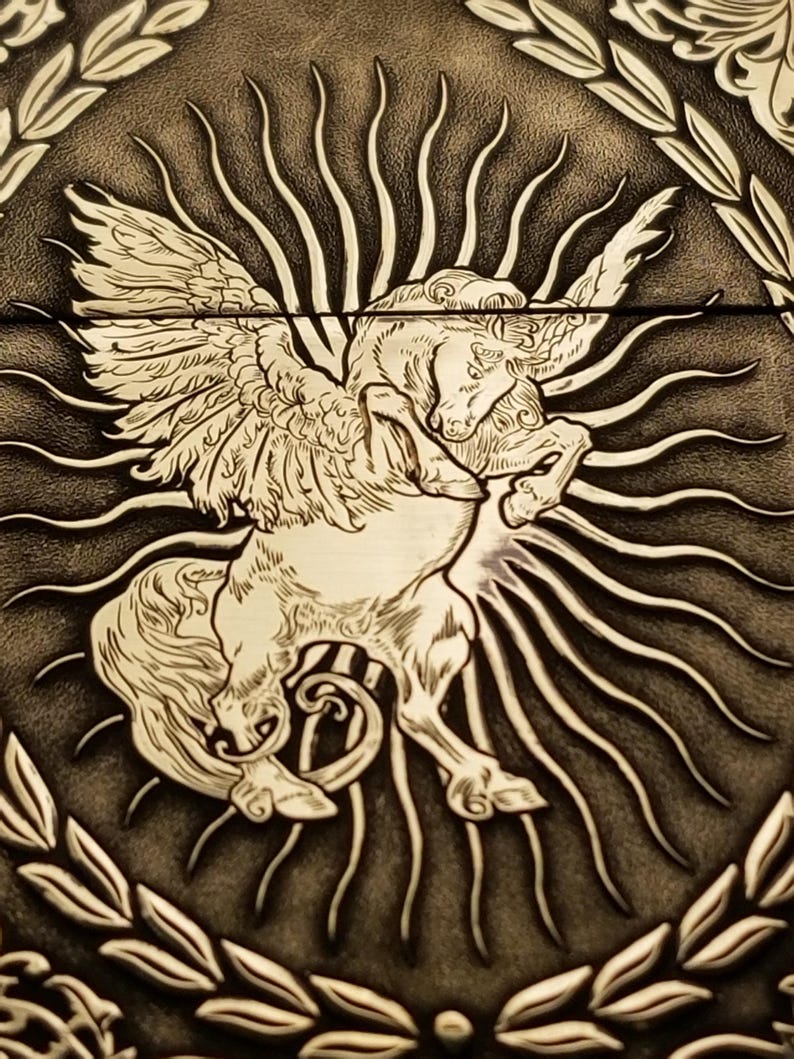 以下が含まれることがあります： 羽根のある馬、またはペガサスを詳細に描いた、エンボス加工された革のデザイン。その背後には太陽の光線が放射状に広がっています。デザインは茶色と白のグラデーションで表現されています。