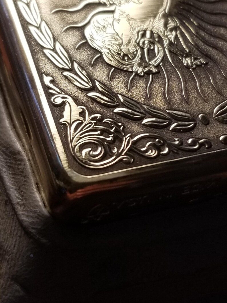 以下が含まれることがあります： 羽根つきの馬と月桂樹の輪のデザインが刻まれた銀色の金属製のタバコケース。ケースの下部には「La  Merveille」という文字が刻まれています。