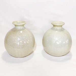 May include: Two spherical glass vases with a narrow neck and a flared rim. The glass has a translucent, off-white, pearlescent finish with a subtle, speckled, or crackled texture throughout the rounded bodies, creating a soft, reflective appearance.