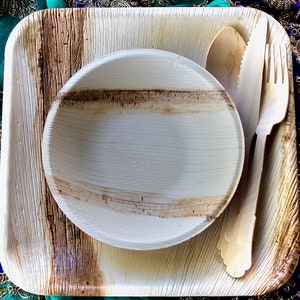 May include: A set of disposable palm leaf plates and cutlery. The set includes a square plate, a round bowl, a fork, and a spoon. The plates and cutlery are made from natural materials and are biodegradable.