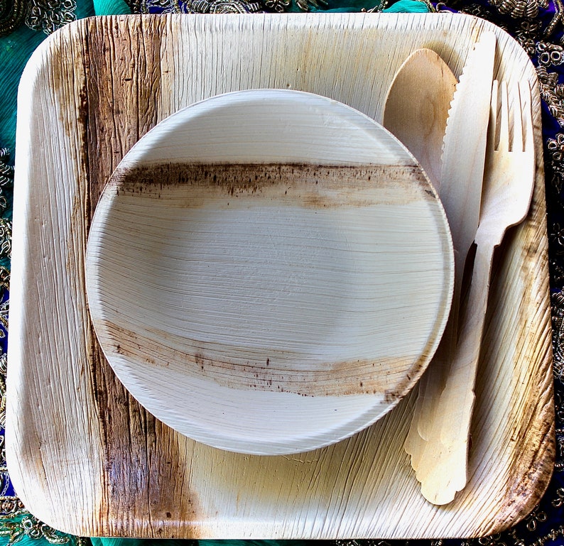 May include: A set of disposable palm leaf plates and cutlery. The set includes a square plate, a round bowl, a fork, and a spoon. The plates and cutlery are made from natural materials and are biodegradable.
