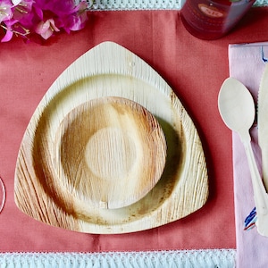 May include: A set of two triangular palm leaf plates, one smaller than the other, on a red tablecloth. The plates are made of natural materials and are perfect for eco-friendly dining.
