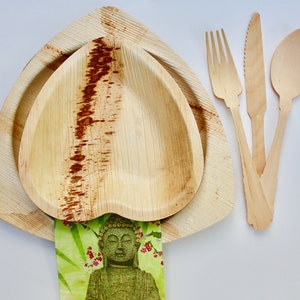 May include: A set of three wooden utensils, including a fork, knife, and spoon, with a heart-shaped palm leaf bowl and a larger, triangular palm leaf plate. The utensils are made of natural wood and have a light brown color. The bowl and plate are also made of natural palm leaf and have a light brown color.