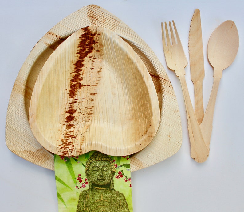 May include: A set of three wooden utensils, including a fork, knife, and spoon, with a heart-shaped palm leaf bowl and a larger, triangular palm leaf plate. The utensils are made of natural wood and have a light brown color. The bowl and plate are also made of natural palm leaf and have a light brown color.