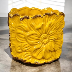 May include: A yellow ceramic planter with a flower design. The planter has a distressed look and is perfect for adding a touch of rustic charm to your home decor.