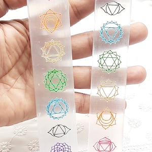 May include: Two clear selenite wands with seven chakra symbols etched on them. The symbols are in different colors, including red, orange, yellow, green, blue, indigo, and violet.