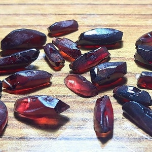 May include: A collection of 20 red and black gemstone roughs. The roughs are in various shapes and sizes, and have a natural, unpolished finish.
