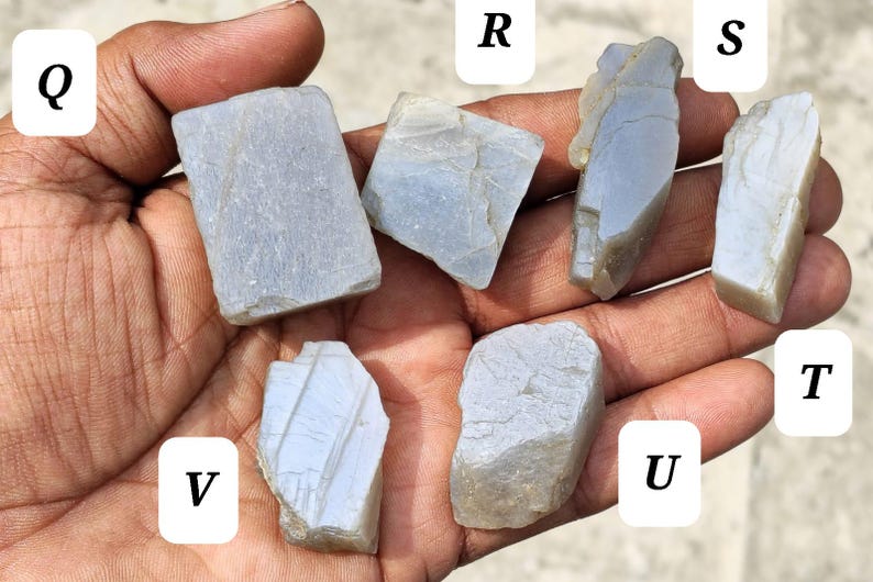 May include: Six rough, light gray, translucent mineral specimens labeled Q, R, S, T, U, and V. Each stone features irregular, angular shapes with visible natural fractures, smooth surfaces, and varying opaque to semi-translucent textures.