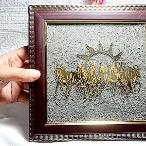 Puede incluir: Obra de arte enmarcada con un sol dorado y caballos. Los caballos están representados corriendo. El marco es de color marrón oscuro y el fondo tiene una apariencia texturizada gris. Adecuado para la decoración del hogar.