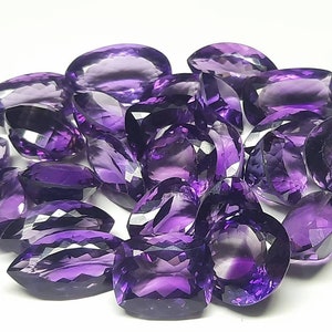 May include: A collection of 17 faceted amethyst gemstones, each with a deep purple hue and a unique, irregular shape.