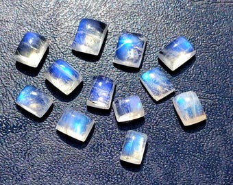 Könnte beinhalten: Eine Ansammlung von elf rechteckigen Mondstein-Cabochons, die jeweils eine glatte, gewölbte Oberfläche mit einem durchscheinenden Aussehen und einem ausgeprägten blauen Schimmer aufweisen, der leuchtet, wenn Licht auf die polierten Edelsteine trifft.