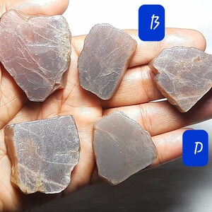 Puede incluir: Cinco piedras preciosas en bruto de color gris con un ligero tono rosado. Las piedras est&aacute;n etiquetadas como A, B, C, D y E.