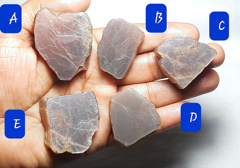 Puede incluir: Cinco piedras preciosas en bruto de color gris con un ligero tono rosado. Las piedras est&aacute;n etiquetadas como A, B, C, D y E.