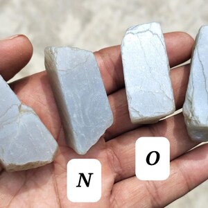 May include: Four rough, pale blue-grey stones labeled M, N, O, and P. Each stone has an irregular, angular shape with visible surface textures, natural cracks, and a matte finish. The stones are presented in a row, showcasing their distinct forms.