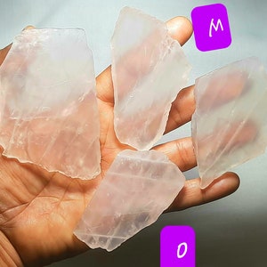 May include: Four pieces of clear, translucent, pink selenite crystal slabs. The slabs are various sizes and shapes. The slabs are labeled L, M, N, and O.