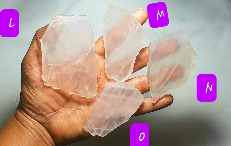 May include: Four pieces of clear, translucent, pink selenite crystal slabs. The slabs are various sizes and shapes. The slabs are labeled L, M, N, and O.