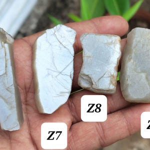 May include: Four rough, pale greyish-blue stones with irregular, fractured surfaces and visible internal veining. Each stone is labeled with a white square containing black text: Z6, Z7, Z8, and Z9, identifying four distinct mineral specimens.