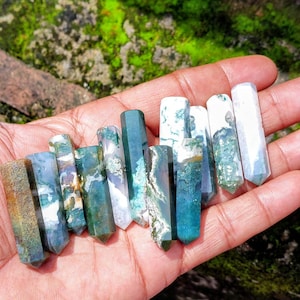 Pode incluir: Uma coleção de dez pontas de cristal de ágata musgo polidas, cada uma apresentando inclusões únicas de padrões minerais em verde escuro, branco e cinza translúcido. Estas torres de pedra hexagonais exibem gradientes de cores naturais variados.