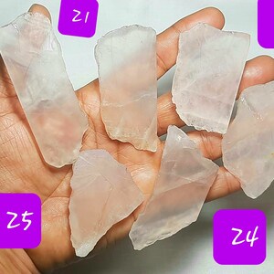 May include: Six pieces of clear, pale pink, translucent, rough-cut, natural rose quartz crystals. The crystals are various sizes and shapes. The crystals are held in a person's hand.