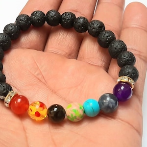Op de afbeelding: Een zwarte lavastenen armband met zeven chakra-parels. De parels zijn rood, oranje, geel, groen, blauw, indigo en violet. De armband heeft gouden spacers met heldere strass-steentjes.