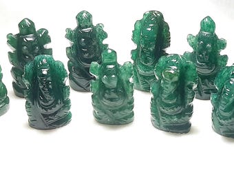 Puede incluir: Una colección de once pequeñas figuras talladas de color verde esmeralda de una deidad, cada una con detalles intrincados. Las figuras están dispuestas sobre una superficie blanca, mostrando su acabado pulido y brillante. Las figuras son del dios hindú Ganesha.