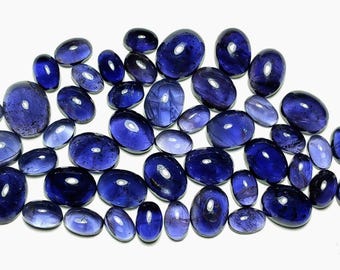 May include: A collection of numerous loose, oval-shaped gemstones in varying shades of deep blue and violet. Each stone features a smooth, polished cabochon cut with a reflective surface, displaying natural colour variations and internal inclusions.