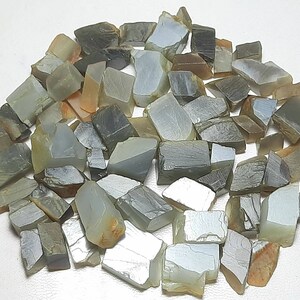 Puede incluir: Una colección de aproximadamente 50 pequeñas piedras preciosas grises y blancas de forma irregular. Las piedras tienen un brillo plateado y están dispuestas en un montón suelto.
