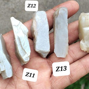 May include: Five rough, translucent, off-white to pale gray mineral specimens labeled Z10, Z11, Z12, Z13, and Z14. Each stone features irregular, jagged edges and a crystalline texture with varying opaque and semi-transparent sections.