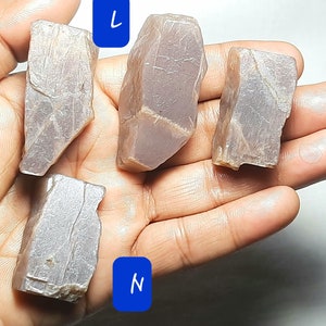 Puede incluir: Cuatro piezas de piedra de sol en bruto, de color p&uacute;rpura claro. Las piedras son de varias formas y tama&ntilde;os. Las piedras est&aacute;n etiquetadas como K, L, M y N.