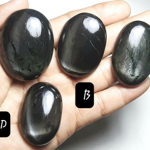 以下が含まれることがあります： A、B、C、Dとラベル付けされた、4つの黒い黒曜石のパームストーン。石は滑らかで磨かれており、わずかに光沢があります。