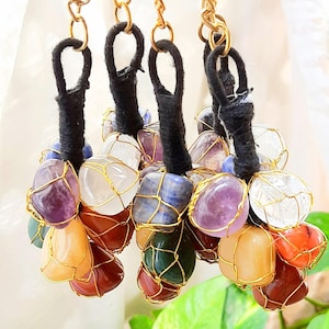 May include: A selection of keyrings with colourful gemstones encased in gold-coloured wire. Each keyring has a black loop and a gold-coloured chain. The gemstones are various colours, including purple, orange, and green.